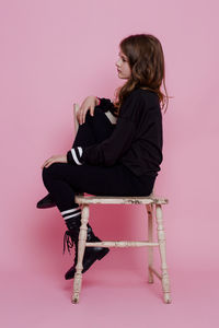 Woman sitting on chair against pink background