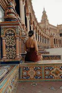 A young woman sitting in front of a historic building - plaza de espana. spanish square