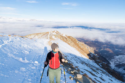 Mature woman skiing on snowcapped mountain against sky