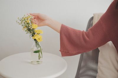 Cropped hand of woman holding flowers in vase on table