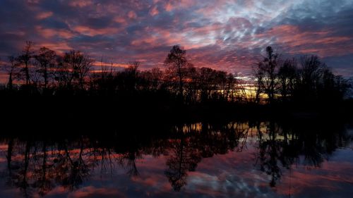 Silhouette trees by lake against sky during sunset