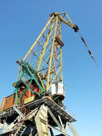 Low angle view of cranes against clear blue sky