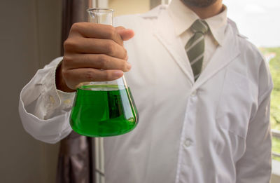 Midsection of scientist holding chemical in beaker