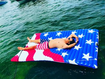 High angle view of shirtless man lying on pool raft over sea