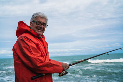 Portrait of man holding fishing rod by sea