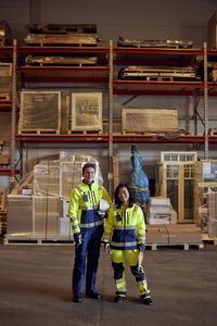 Portrait of confident female colleagues in reflective clothing standing at distribution warehouse