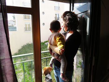 Mother carrying son while looking through balcony