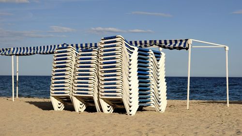 Hooded chairs on beach against sky