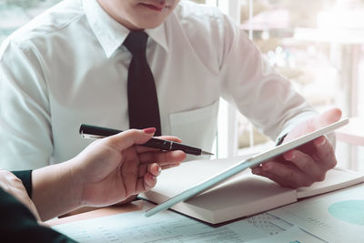 Midsection of businessman holding digital tablet while discussing with female colleague at desk in office