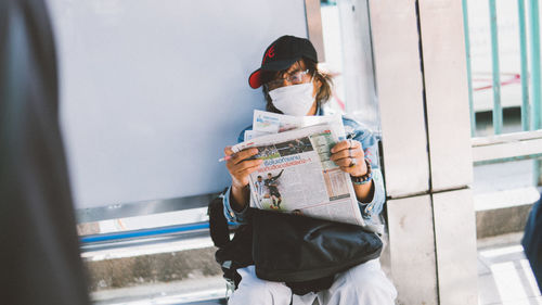 Woman reading book while sitting on window