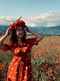 Woman wearing red flower standing on field against sky