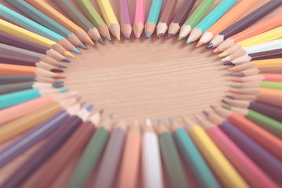 Close-up of colored pencils arranged in circle shape on wooden table