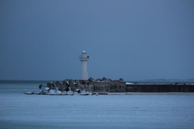 Lighthouse by sea and buildings against sky