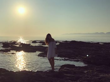 Woman standing at beach against sky during sunset