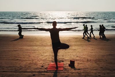 People exercising on beach during sunset