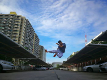 Boy jumping on road in city against sky