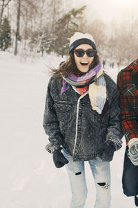 Cheerful woman standing with friend on snow covered landscape