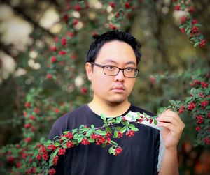 Portrait of young man wearing eyeglasses and holding red rowan berries branch against rowan tree.