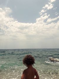 Rear view of shirtless boy looking at sea against sky