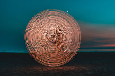 Illuminated lighting equipment on beach against sky at sunset