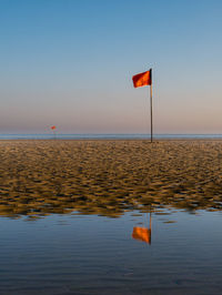 Red flag mirroring in water just after sunrise at a beach in northern france