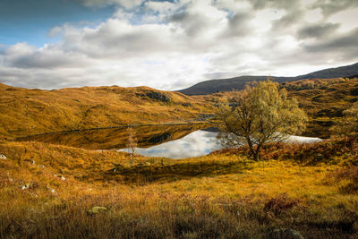 Scenic view of lake on landscape against cloudy sky