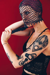 Woman covering face with net scarf against red background