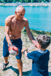 Shirtless grandfather with grandson boxing by swimming pool