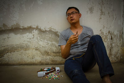 Mid adult man with drugs sitting on floor against wall