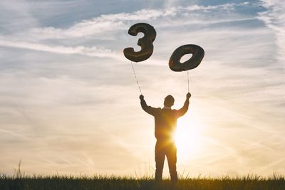 Low angle view of man holding number 30 helium balloons against sky