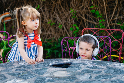 Cute boy listening music with sister at table