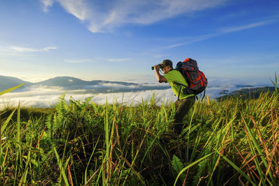 Hiker with backpack standing looking through binoculars on the mountain