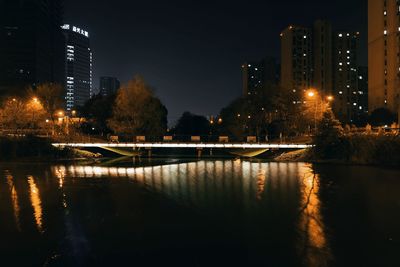 Illuminated buildings by river against sky at night