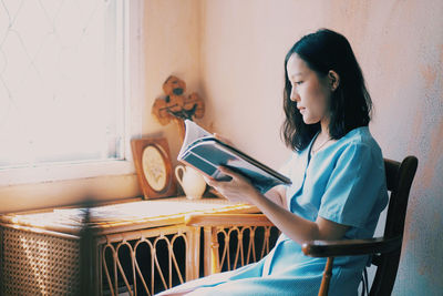 Woman sitting on chair against wall