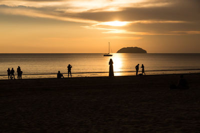 Silhouette people on beach against sky during sunset