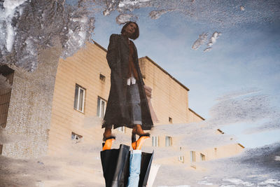 Reflection of a woman posing in front of generic building, full