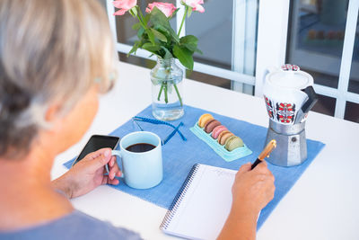 Woman having coffee while writing in book at home