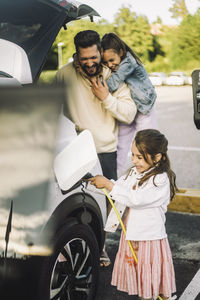 Happy father with daughters charging electric car at station