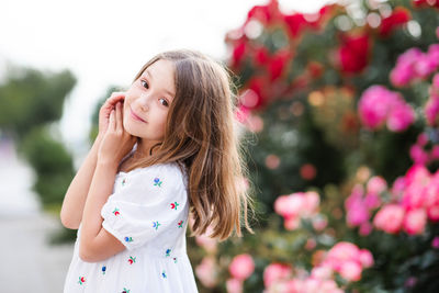 Happy adorable little kid girl 7-8 year old stand in park garden over bloom bushes of rose flower