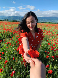 Beautiful young woman holding red poppy flowers in field