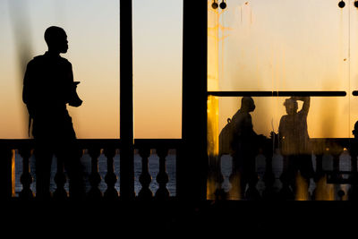 Silhouette people standing by railing against orange sky