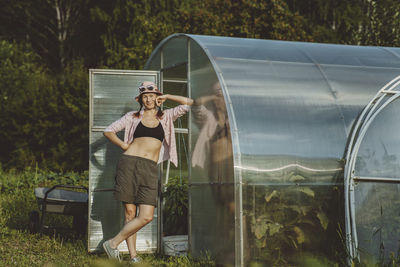 Smiling farmer standing with legs crossed at knee by greenhouse