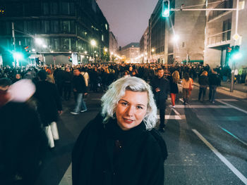 Portrait of smiling young woman standing on crowded street at night