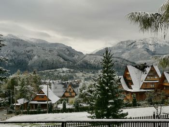 Houses and trees on snowcapped mountains against sky