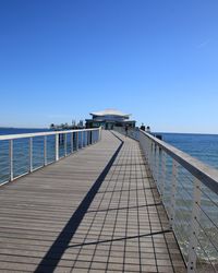 Pier over sea against clear blue sky
