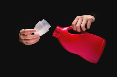 Cropped hand holding bottle against black background