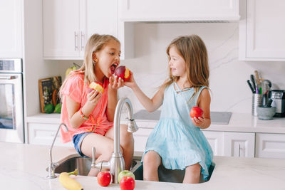 Caucasian children girls eating sharing fresh fruits sitting in kitchen sink. happy family sisters 