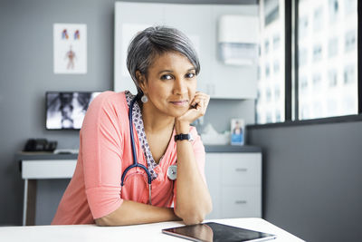 Portrait of confident female doctor leaning on desk in clinic