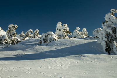 Snow covered land against clear blue sky