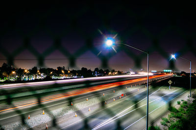 Light trails on street seen through fence at night